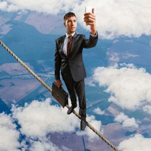 A accountant is standing on a tight rope while holding up his phone
